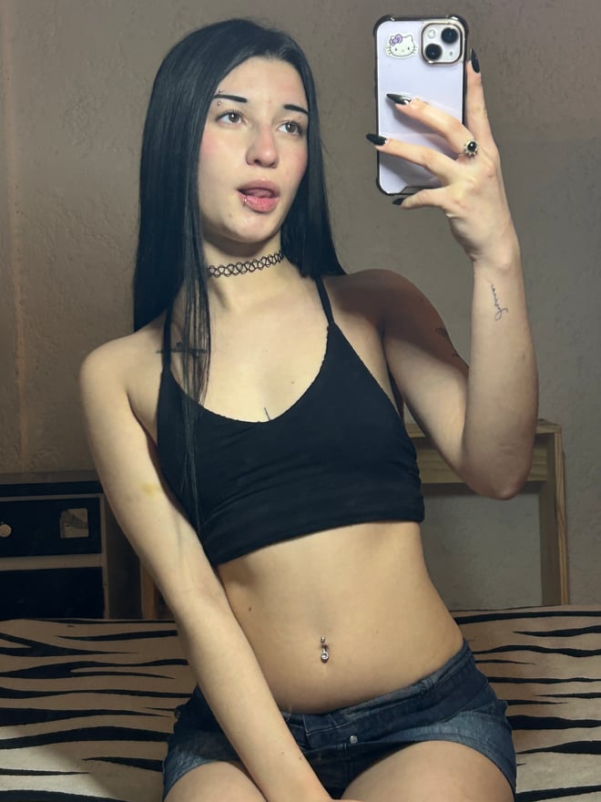 A person with dark hair taking a selfie in a bedroom setting.