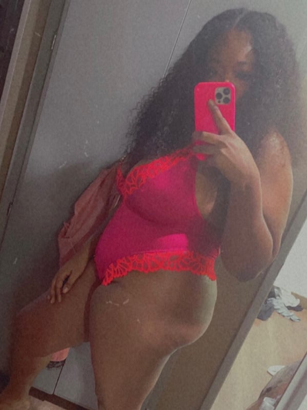 Person posing in a pink outfit while holding a phone for a selfie in front of a mirror.