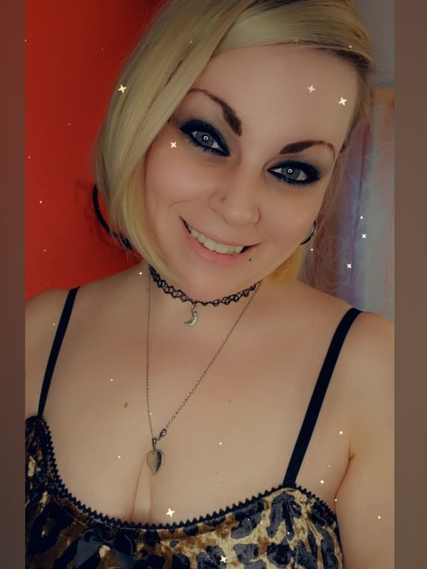 A smiling woman with blonde hair and dramatic makeup poses in a leopard print top against a red background.