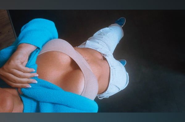 A woman posing on the floor in a light blue cardigan, beige top, and white pants with blue shoes, viewed from above.
