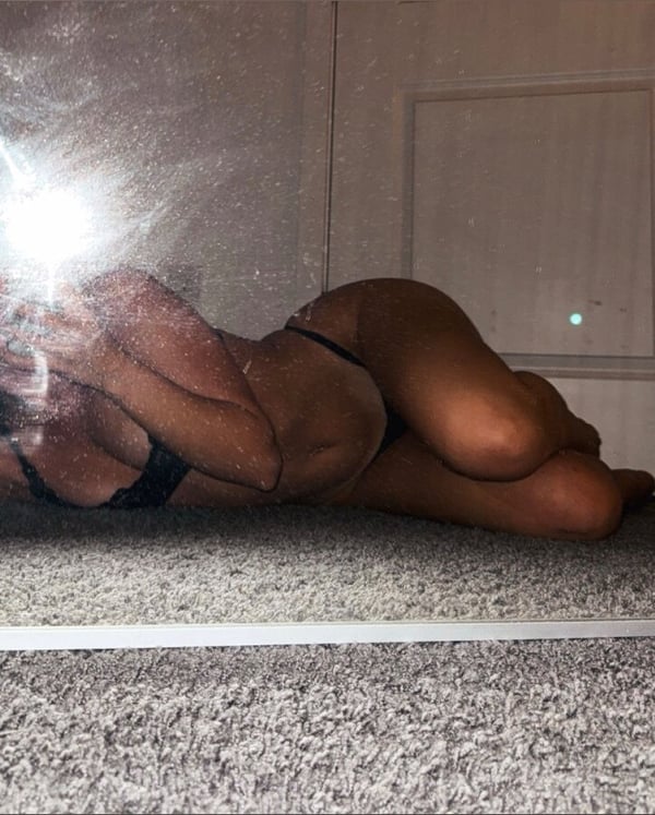 A woman lying on the floor in a bedroom, captured in a mirror selfie wearing lingerie.