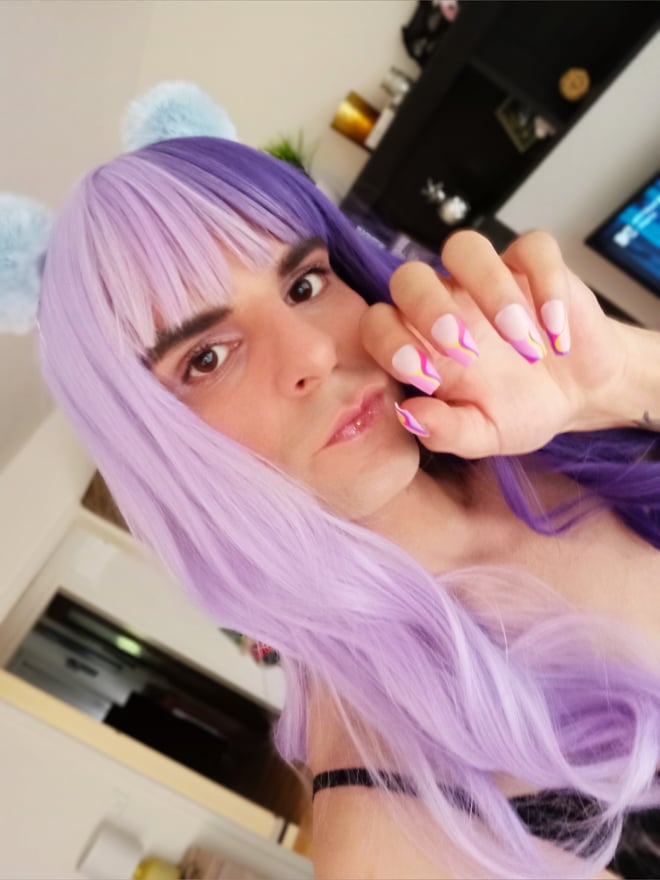 Person with split purple and pink wig and cat ears posing indoors with manicured nails.
