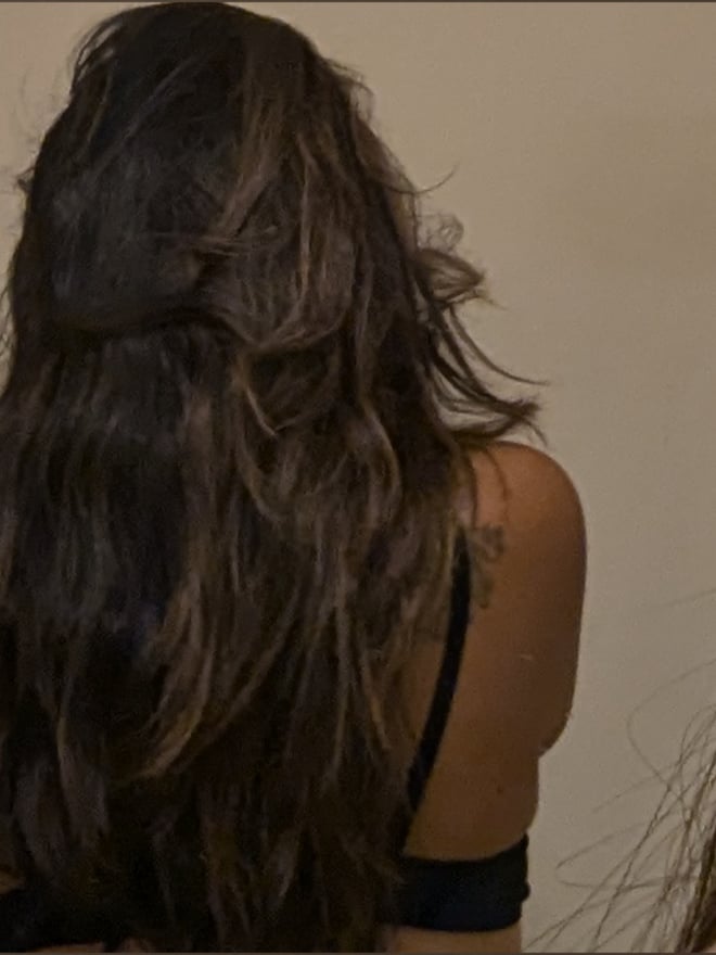 A woman standing in a bathroom, looking at her phone while wearing dark lingerie.