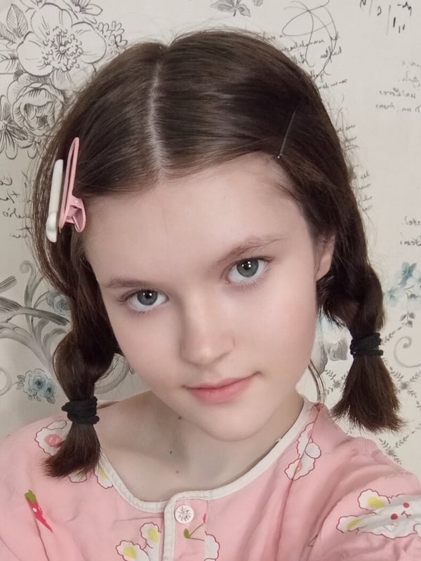 Close-up portrait of a young woman with brown hair styled in pigtails with colorful clips, wearing a pink top.
