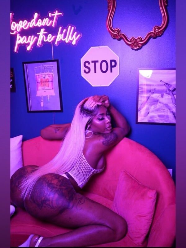 A woman lounging on a red chair in a vibrant purple room with neon signs and eclectic decor.