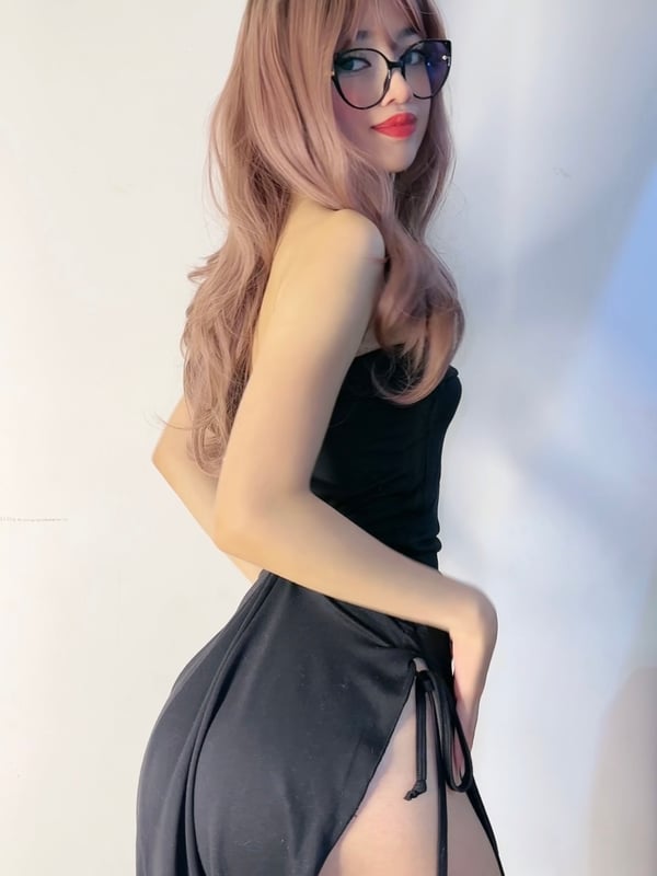 A person with long brown hair wearing a black lace top, posing indoors.