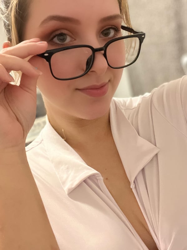 A woman with glasses and blonde hair smiling at the camera while wearing a white top.