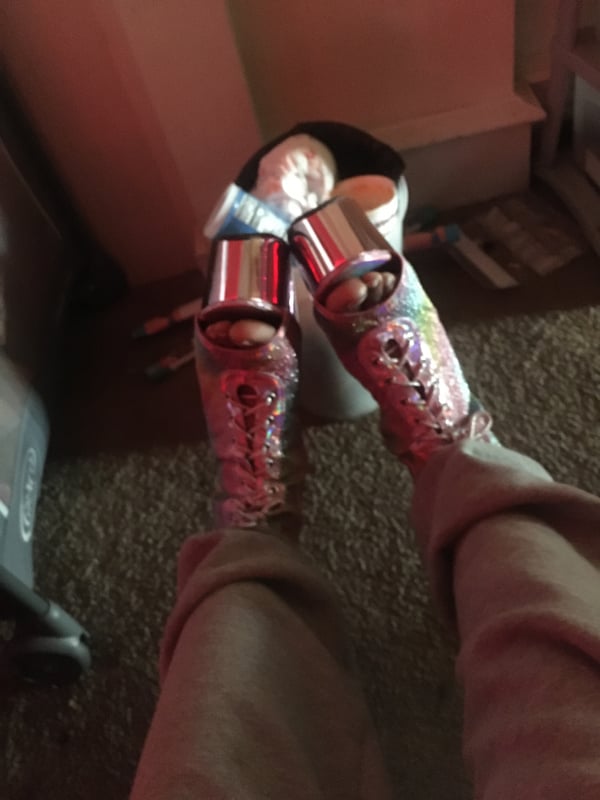 Close-up view of a person's legs wearing sparkly high-heeled shoes next to a trash bin in a room.