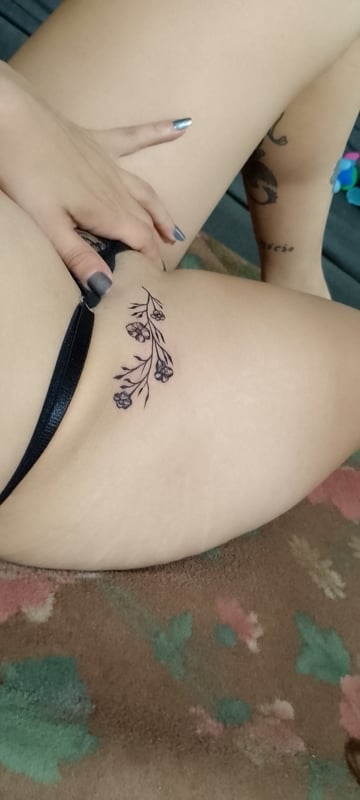 A person lounging on a colorful rug, showing off a floral tattoo on their thigh while wearing dark underwear.