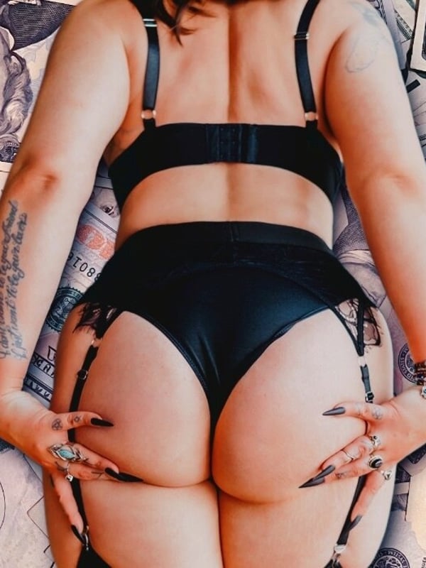 A woman posing from behind in black lingerie surrounded by scattered US dollar bills.