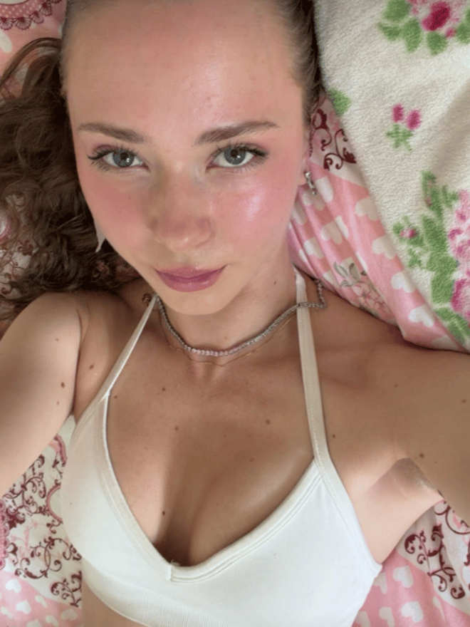 A young woman with brown hair poses for a close-up portrait while reclining on a floral bedspread.