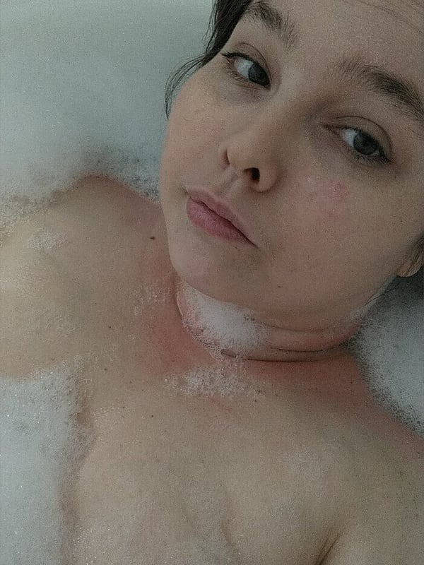 A woman relaxing in a bubble bath with wet hair, looking towards the camera.