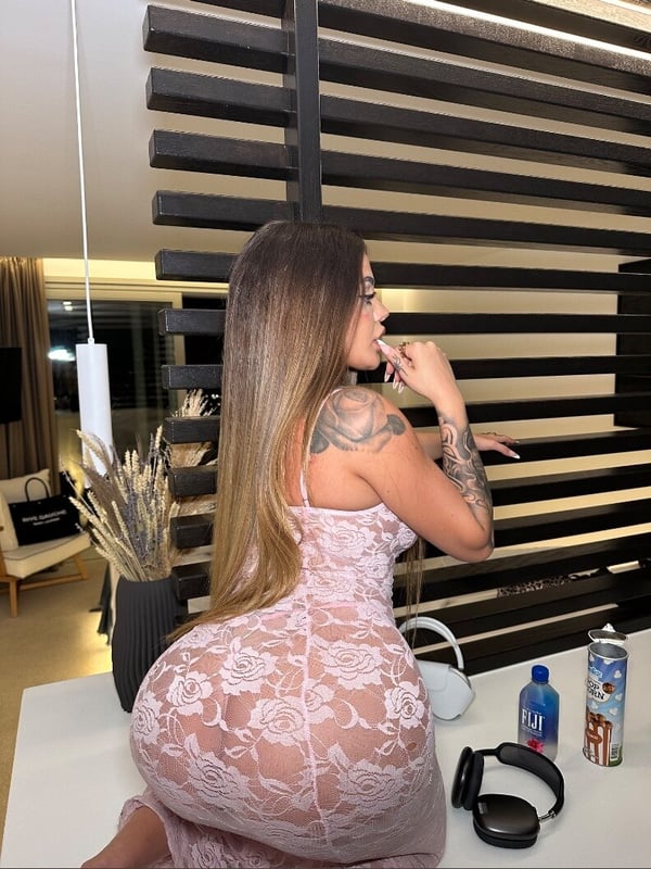 A woman with long hair posing thoughtfully in a sheer dress inside a modern room with wooden partitions and decor.