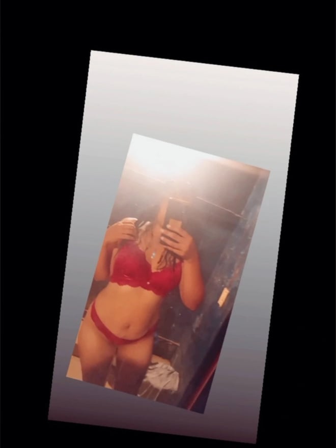A woman taking a mirror selfie in a red bikini, standing in a bathroom setting.