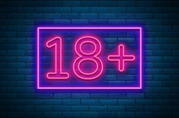 Neon pink '18++' sign glowing against a dark brick wall background.