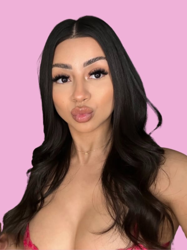 A woman with long dark hair and bold makeup posing with puckered lips against a pink background.