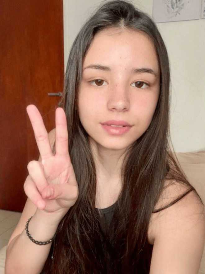 A young woman with long dark hair posing in black lace clothing against white bedding.