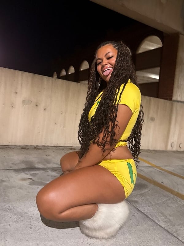 Young woman with long curly hair smiling while sitting on the ground in a yellow outfit at night in a parking structure.