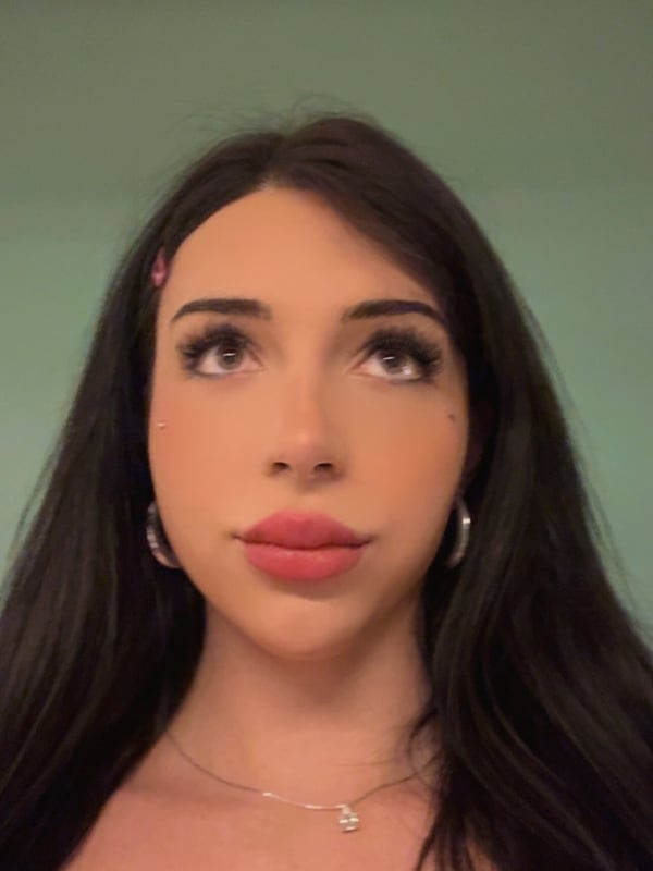 Close-up portrait of a person with long dark hair and makeup against a plain background.