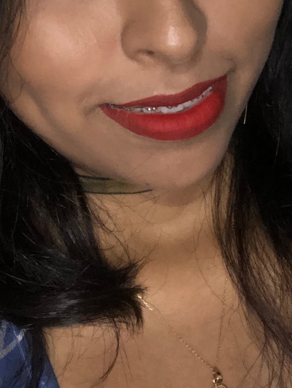 Close-up portrait of a woman with long dark hair, red lipstick, and a necklace, smiling confidently.