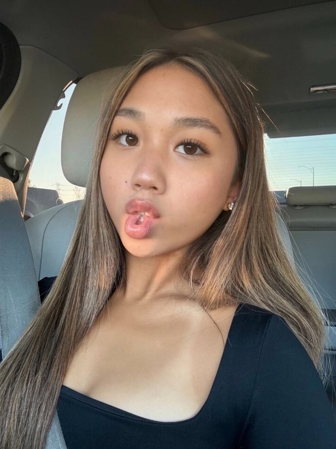 A young woman with long hair taking a selfie inside a car.