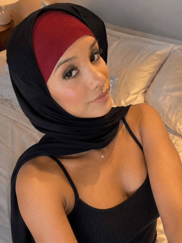 A close-up selfie of a woman wearing a hijab, posing indoors with her hand near her face.