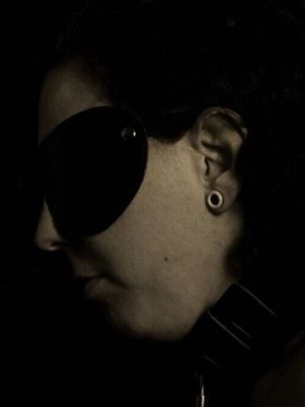 Close-up portrait of a woman with red hair wearing large sunglasses and a choker necklace in black and white tones.