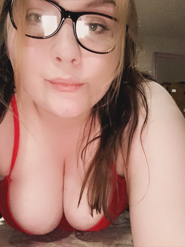 Young woman with glasses wearing a red top, smiling at the camera indoors.