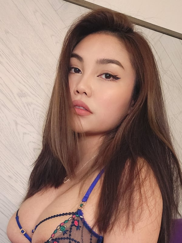 Woman with long dark hair wearing lace lingerie, posing confidently indoors with a neutral expression.