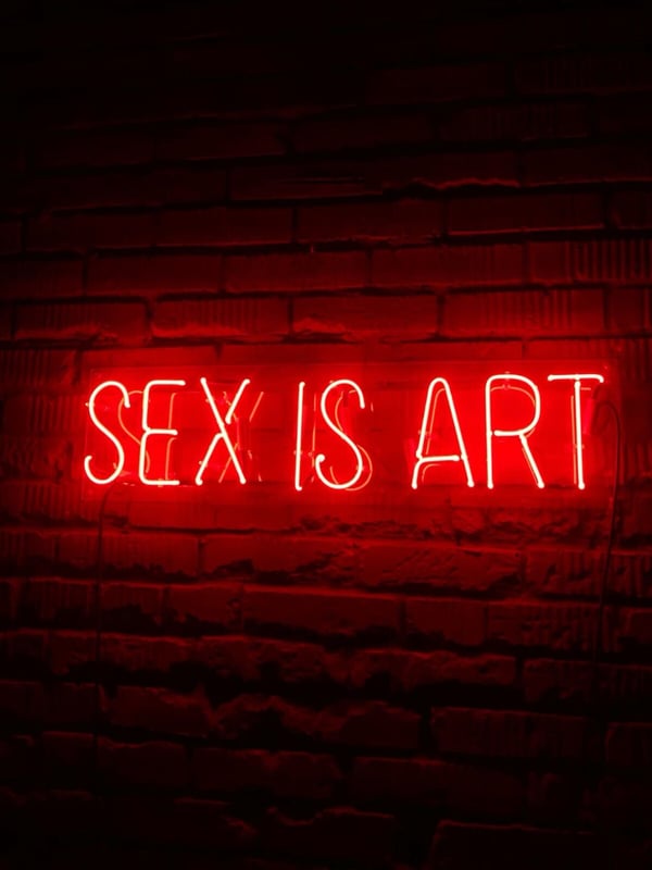 Neon sign on a brick wall reading 'SEX IS ART' in bold red letters.