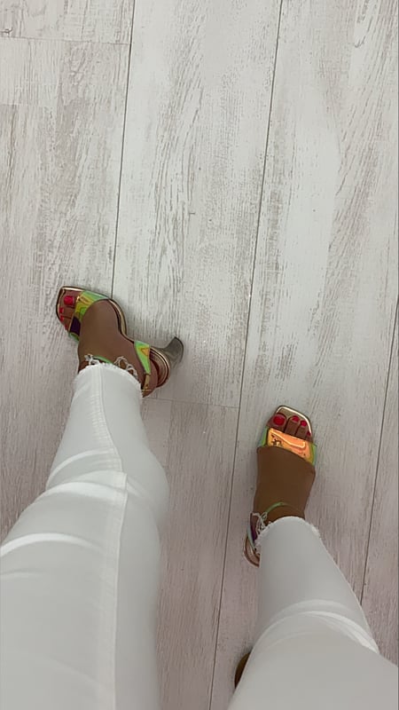 Close-up view of a person's feet wearing colorful high-heeled sandals standing on a light wooden floor.
