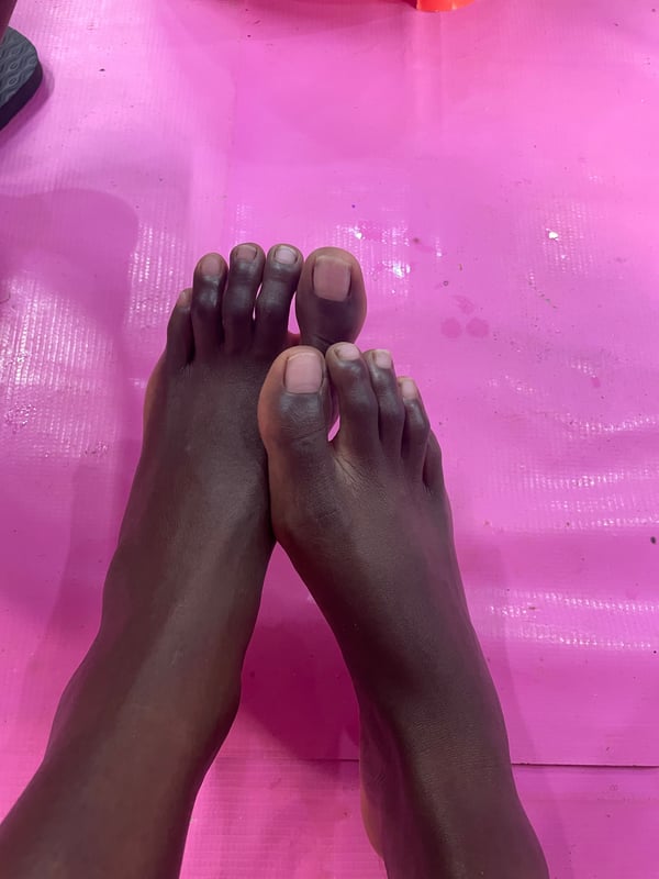Close-up of dark-skinned bare feet posed on a pink surface with some water droplets.