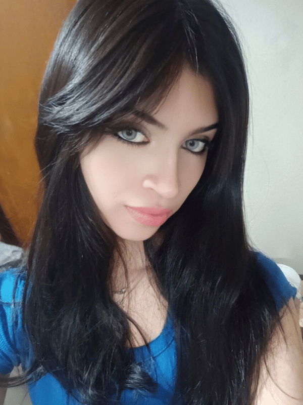 A close-up selfie of a person with long dark hair wearing a blue top in an indoor setting.