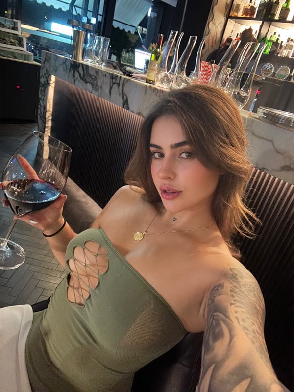 A person holding a glass of red wine while seated at a bar counter.