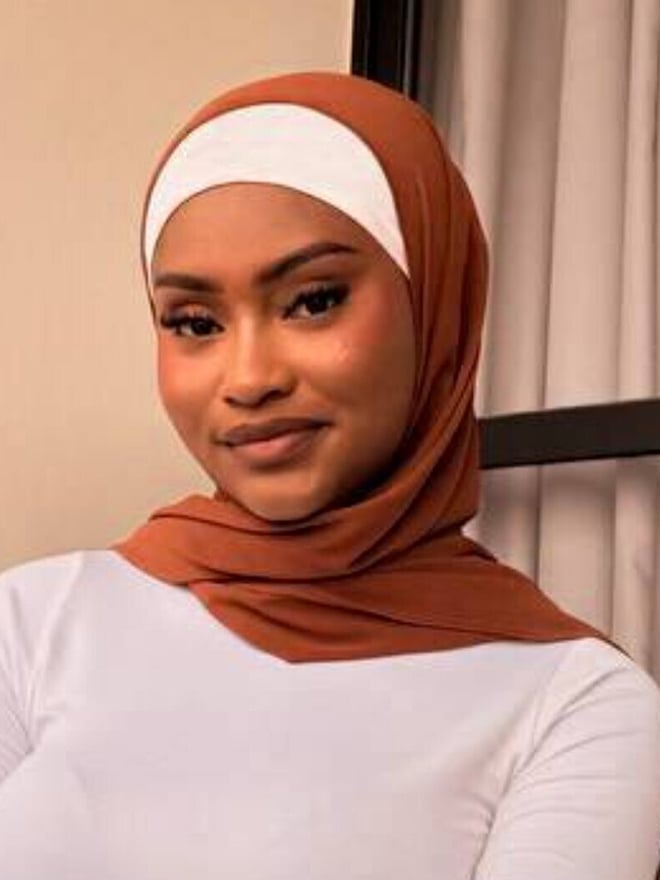 Portrait of a woman wearing a brown headscarf and white headband against an indoor background.