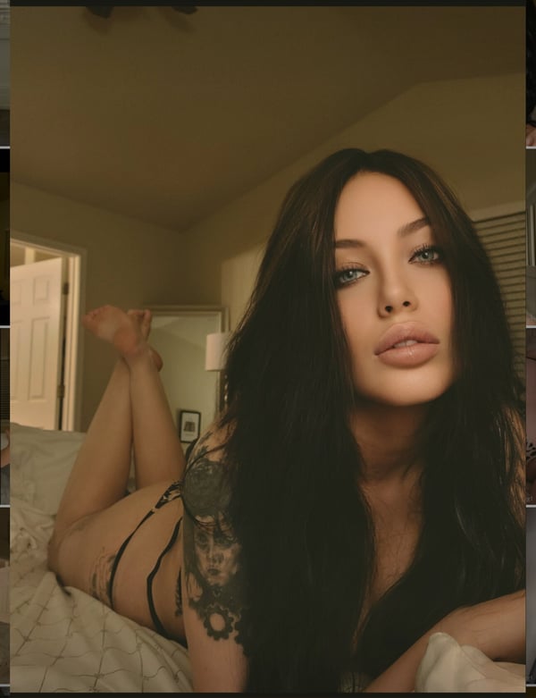 A woman with long dark hair reclining on a bed in a warmly lit room, wearing minimal attire and displaying tattoos.