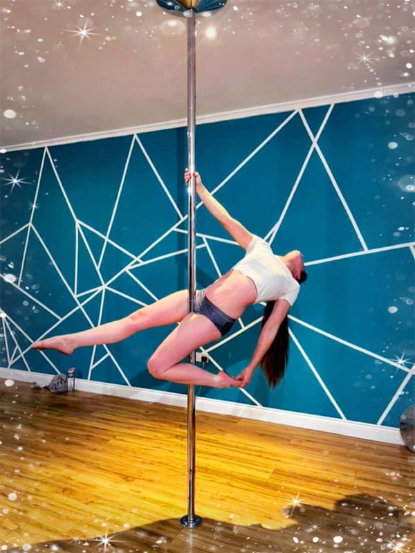A woman posing dynamically on a pole against a geometric blue wall in a studio with sparkling effects.