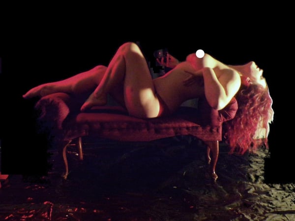 A woman reclining on a fur blanket in a dimly lit room with wooden decor, wearing red lace lingerie.