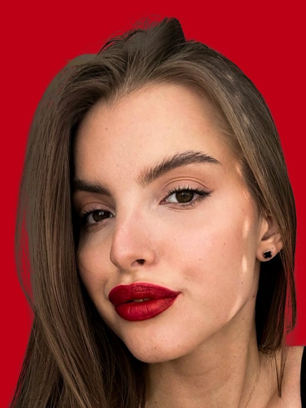Close-up portrait of a woman with long brown hair, red lipstick, and earrings against a red background.