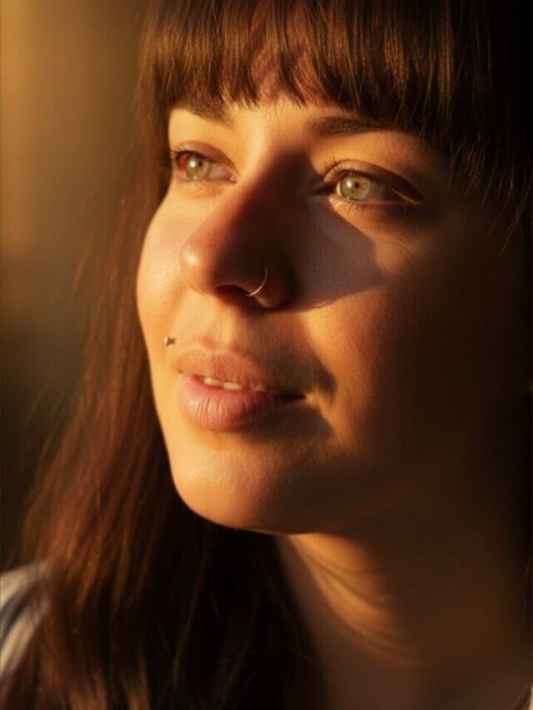 Close-up portrait of a young woman with long brown hair and bangs, smiling softly in warm lighting.
