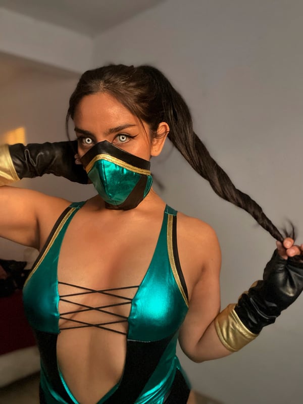 A woman in a shiny green costume with mask and gloves poses confidently, showing her face and ponytail.