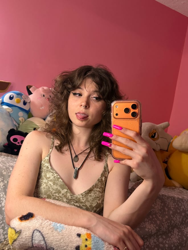 A woman posing in a red-and-black themed costume with thigh-high boots in a colorful bedroom.