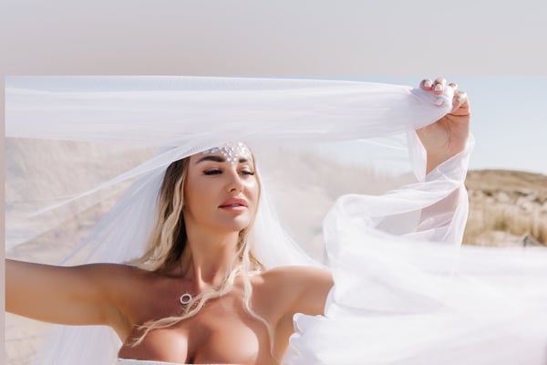 A woman in a white veil posing outdoors in a desert landscape under bright sunlight.