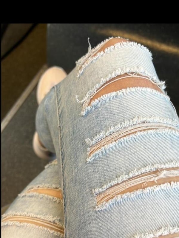 Close-up view of a person's legs wearing distressed light blue jeans with rips, posed on a dark surface.
