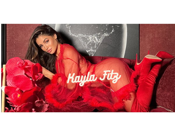 Woman posing seductively on a red velvet couch in a sheer red feathered outfit and high boots, surrounded by orchids, with her name overlaid.