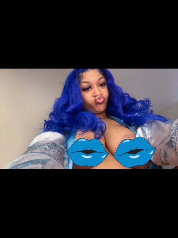 Close-up of young woman with blue hair making a playful expression while wearing a translucent top.