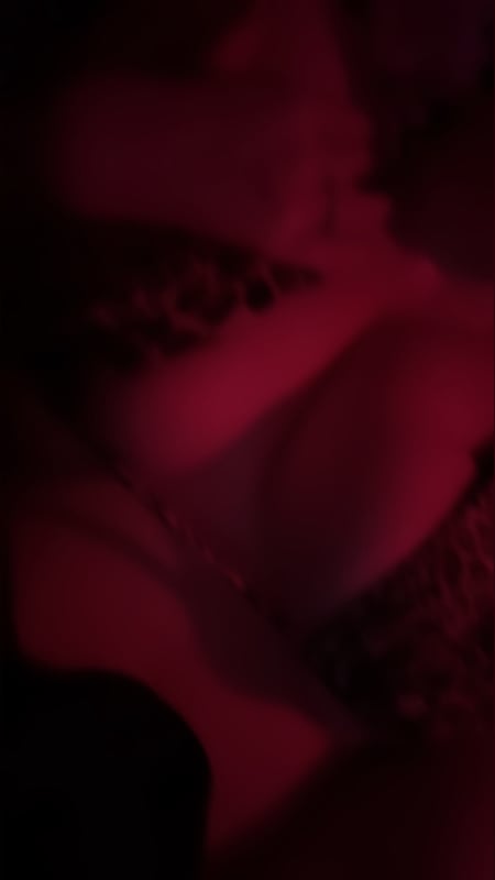 A close-up portrait of a young woman with long hair in a dimly lit room with red lighting and subtle patterns in the background.