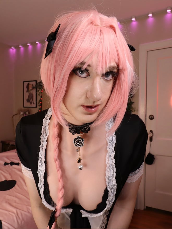 Person with pink hair and cat ears wearing a black and white maid outfit, posing in a bedroom with pink lighting and neon fox sign.
