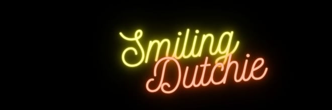 Neon sign displaying 'Smiling Dutchie' in yellow and pink glowing letters against a dark background.
