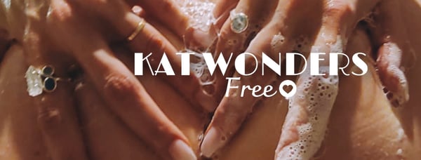 Hands adorned with rings and soap suds forming a heart shape around the text 'KAT WONDERS FREE'.